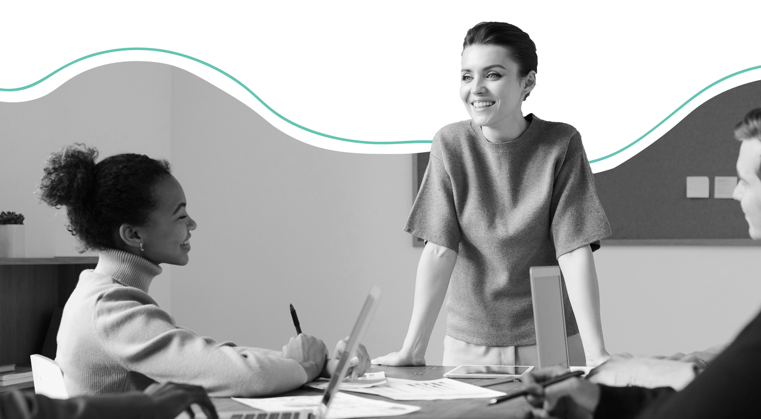 two women at a desk, one standing, one sitting, both smiling and discussing work