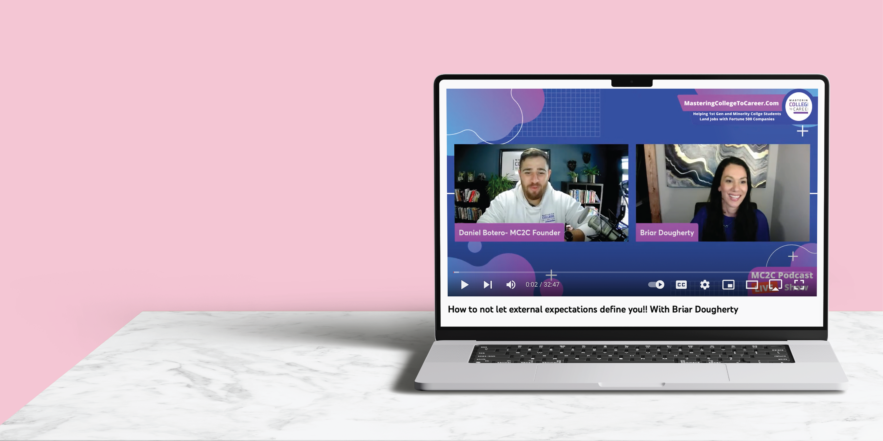 laptop and marble table with screen showing a virtual webinar with a man and a women, pink background